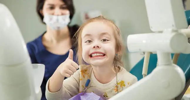 Girl in dental chair giving thumbs up.