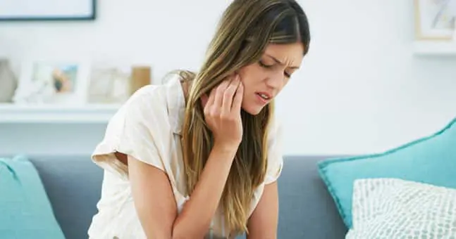 Girl holding her jaw in pain sitting on blue couch.