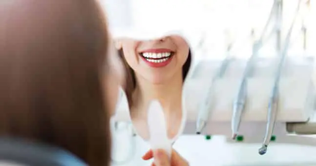 Woman smiling in mirror with new porcelain veneers.