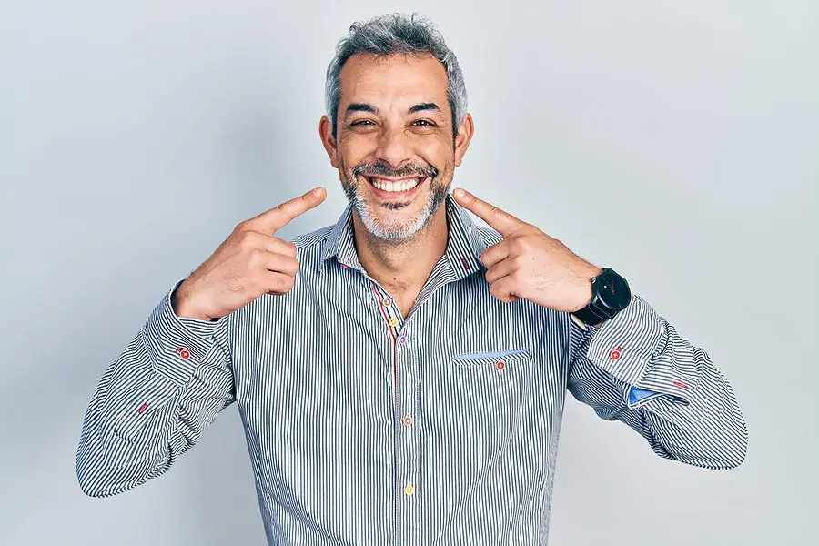 Handsome middle age man with grey hair pointing mouth with finge