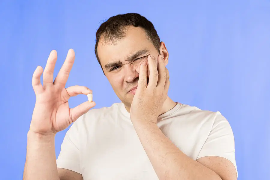 Man In A White T-shirt On A Blue Background Holds A Wisdom Tooth