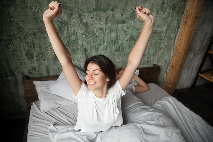 Young Smiling Woman Waking Up Happy After Healthy Sleep Stretchi
