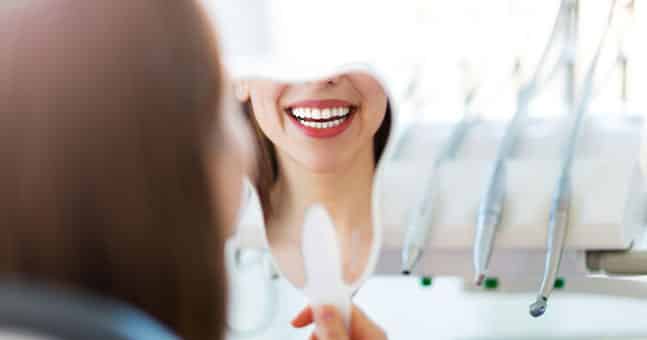 Woman smiling in mirror with new porcelain veneers.