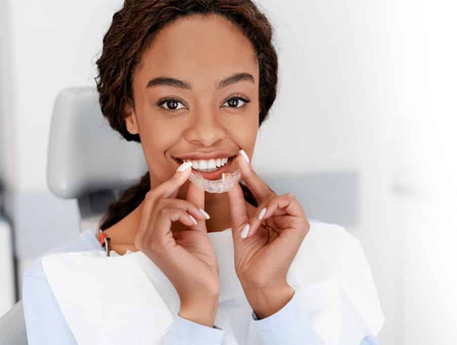 Black woman holding clear braces at Clinton Dental Center.