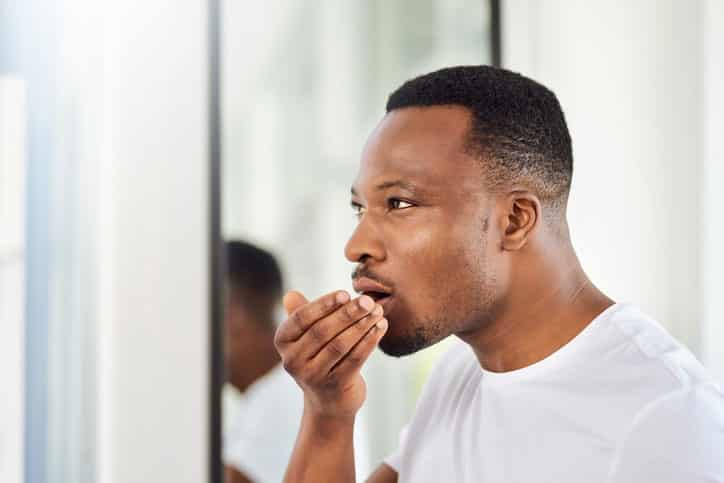 Black man checking breath in morning.