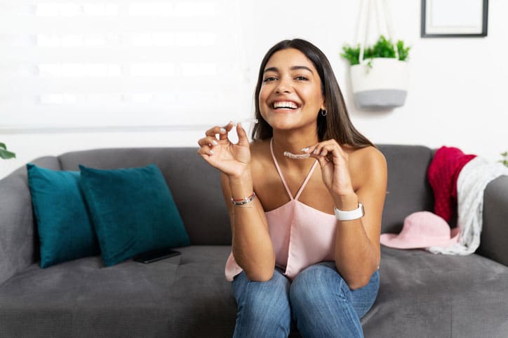 Portrait of a beautiful Hispanic woman looking happy and smiling while holding a couple of dental retainers for her orthodontics treatment