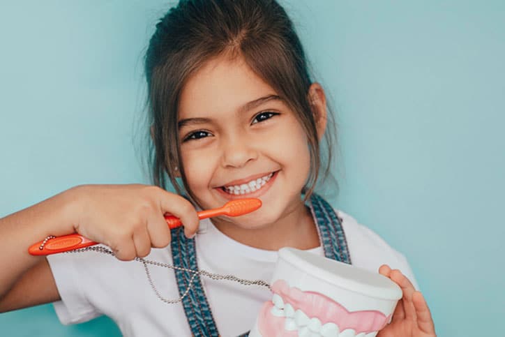 smiling mixed raced girl brushing teeth at blue background.