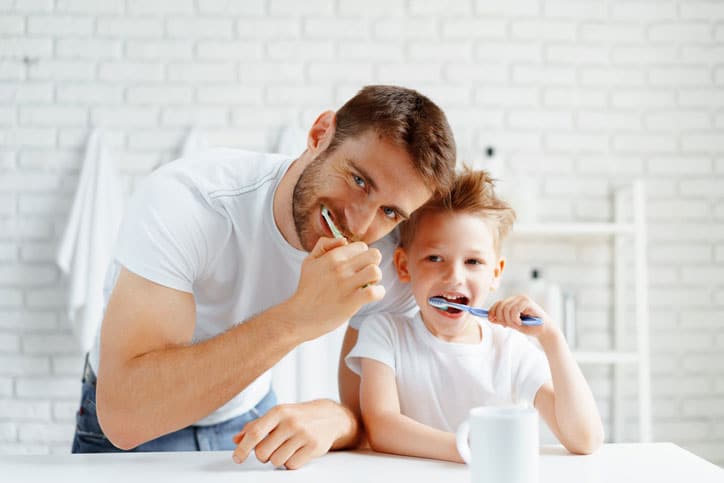 Dad and little son brushing teeth together in bathroom